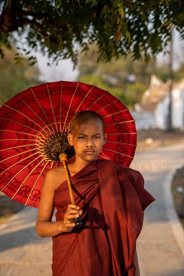 Buddhist monk stands with red umbrella on a path