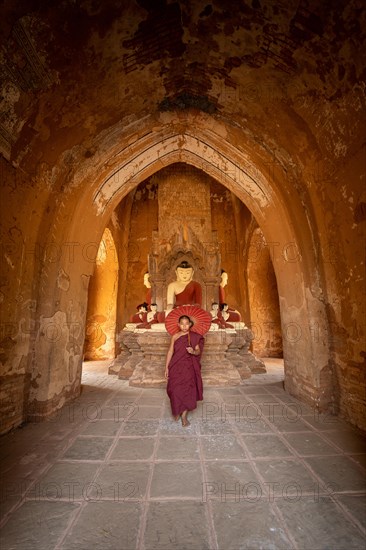 Buddhist young monk in red robe with red umbrella walks in a temple