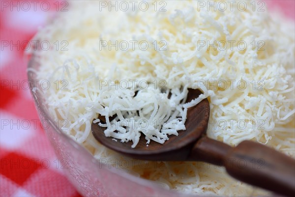 Grated Parmesan cheese in glass bowl with wooden spoon