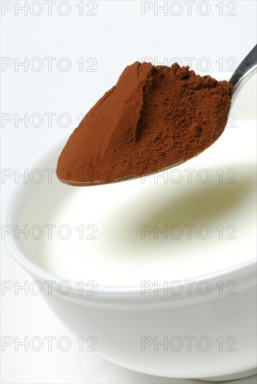Spoon of cocoa powder is put into cup with milk