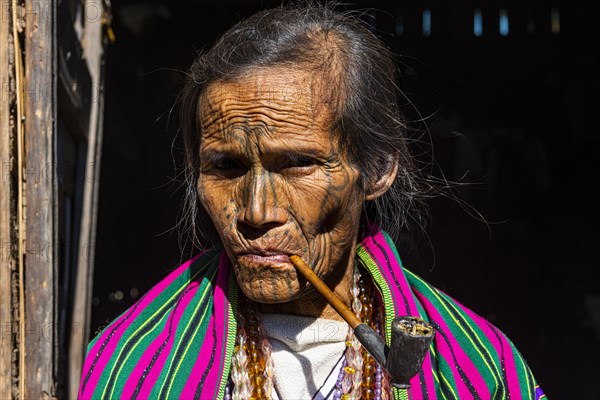 Chin woman with spiderweb tattoo smoking a pipe
