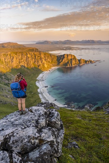 Hiker standing on a rocky outcrop overlooking beach and sea