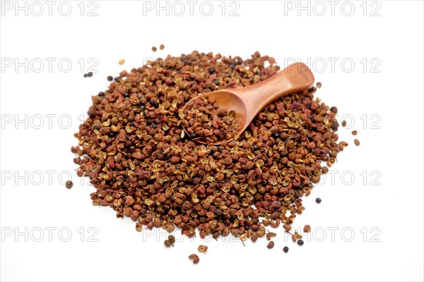 Sichuan peppercorns with a wooden spoon against a white background