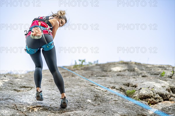 A woman climbing a steep rock using climbing harness