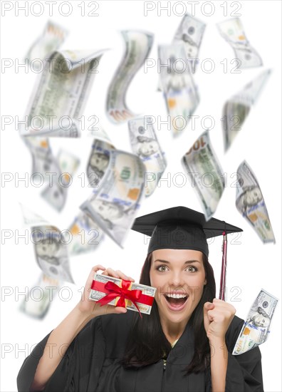 Excited female graduate in cap and gown holding stack of $100 bills with many falling around her on white
