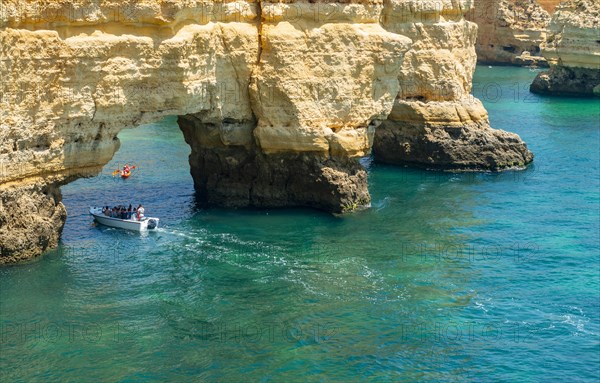Excursion boat sails through rock arch in turquoise sea
