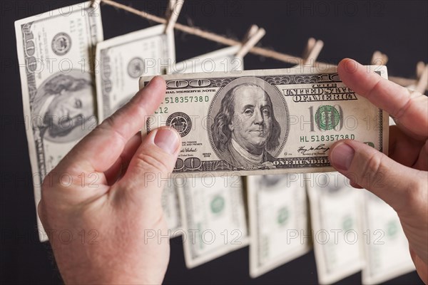 Male hands holding hundred dollar bills with several hanging from a clothesline on a dark background