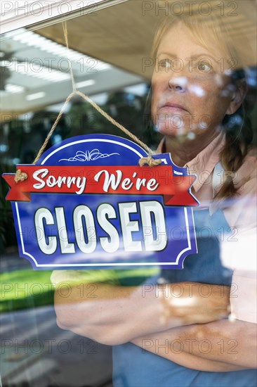 Sad female store owner turning sign to closed in window