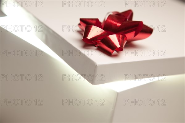 Gift box with red bow lid revealing very bright contents on a gradated background