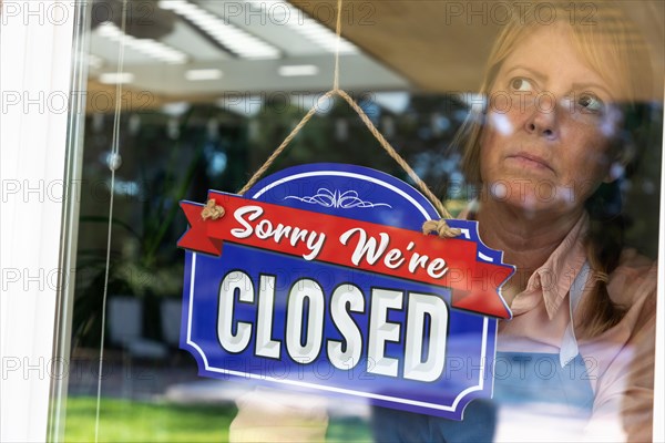 Sad female store owner turning sign to closed in window