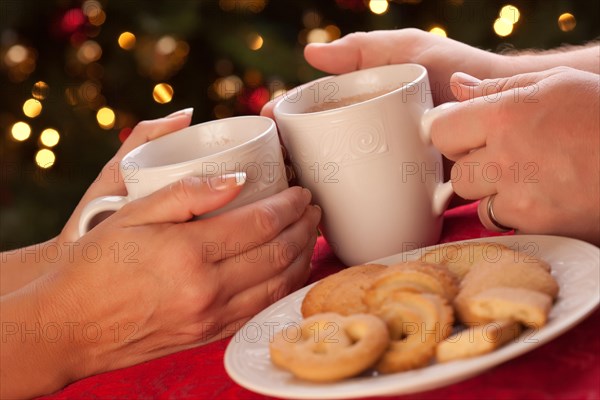 Man and woman sharing hot chocolate and cookies in front of holiday lights