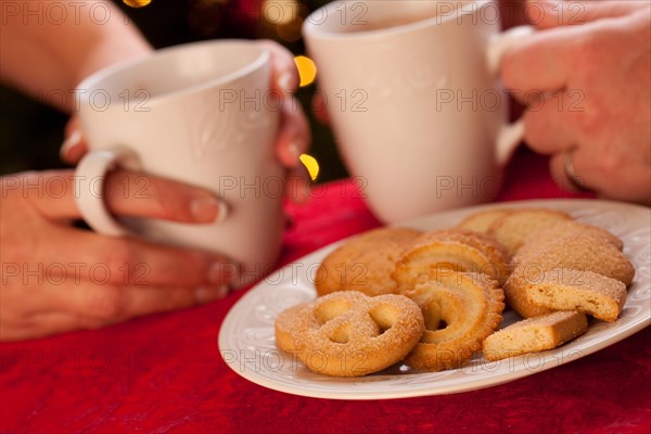 Man and woman sharing hot chocolate and cookies in front of holiday lights