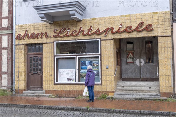 A woman stands in front of the shop window of the former cinema in Doemitz
