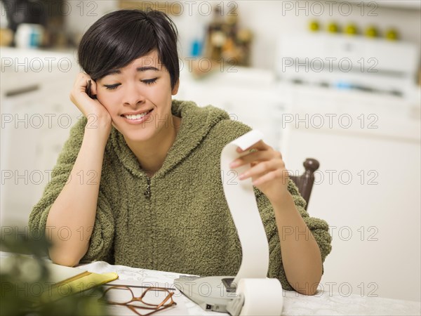 Multi-ethnic young woman relieved and smiling over financial calculations in her kitchen