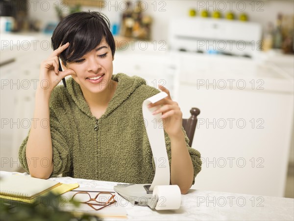 Multi-ethnic young woman relieved and smiling over financial calculations in her kitchen