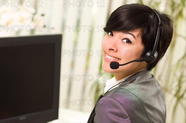 Attractive young woman smiles wearing headset near her computer monitor