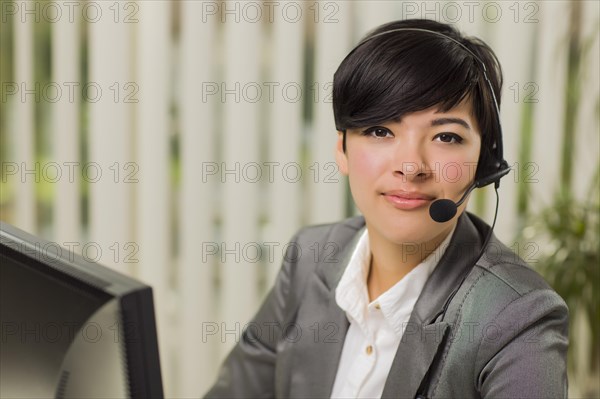 Attractive young mixed-race woman smiles wearing headset near computer monitor