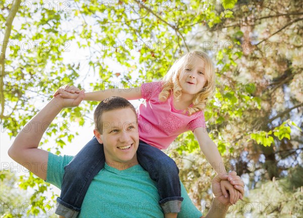 Cute young girl rides piggyback on her dads shoulders outside at the park