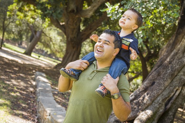 Happy mixed-race son enjoys a piggy back ride in the park with dad