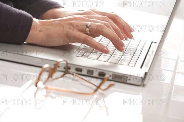 Female hands typing on the keyboard of the laptop with eyeglasses nearby