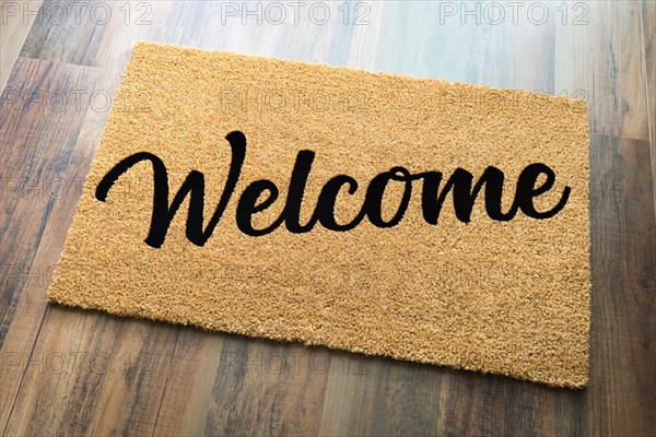 Tan welcome mat on wood floor background