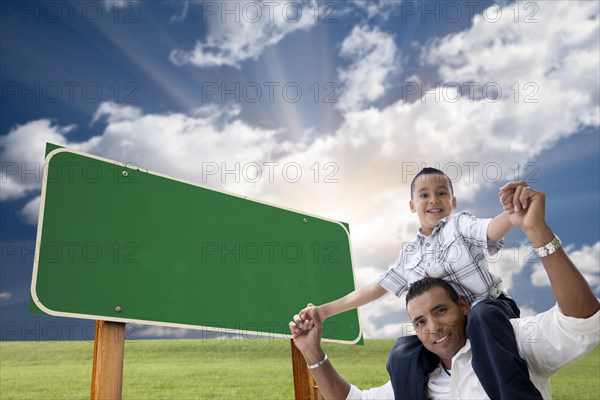 Attractive happy hispanic father and son in front of blank green road sign ready for your own message