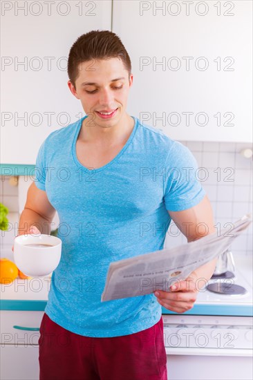 Young man reading newspaper in kitchen morning laugh in Germany