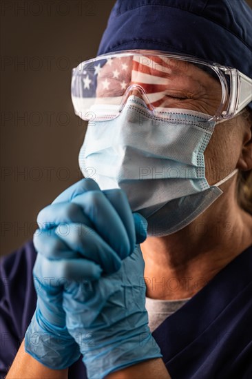 American flag reflecting on distressed praying female medical worker wearing protective face mask and goggles