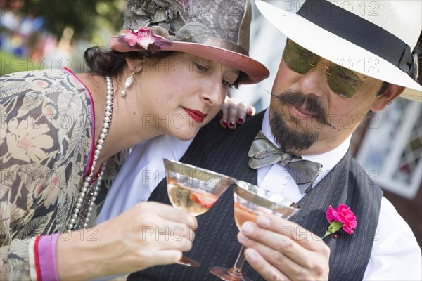 Attractive mixed-race couple dressed in 1920's era fashion sipping champagne