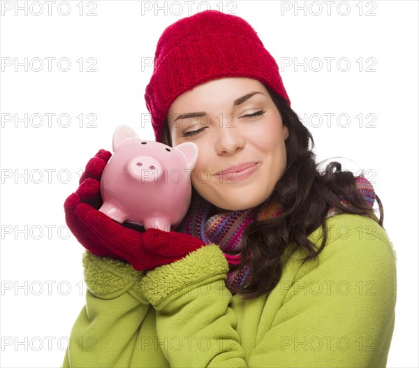 Pleased mixed-race woman wearing winter clothing hugging piggybank isolated on white background