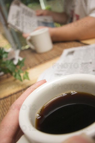 Morning coffee macro of cup with man reading newspaper in background