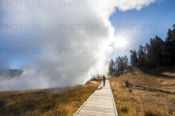 Hiker on footbridge next to steaming hot spring
