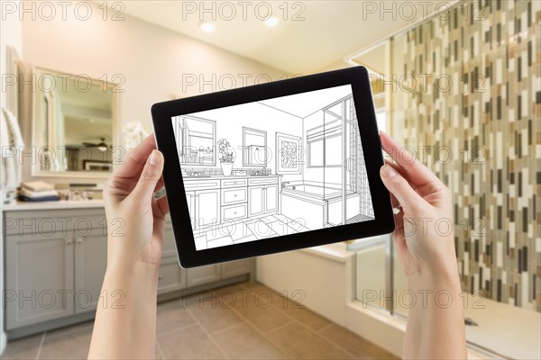 Hands holding computer tablet with master bathroom drawing on screen and photo behind