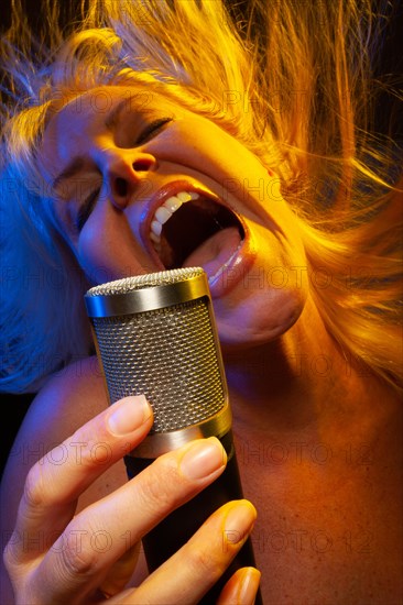 Female vocalist under gelled lighting sings with passion into condenser microphone