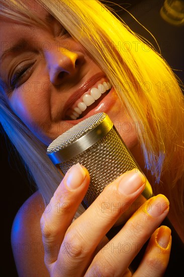 Female vocalist under gelled lighting sings with passion into condenser microphone