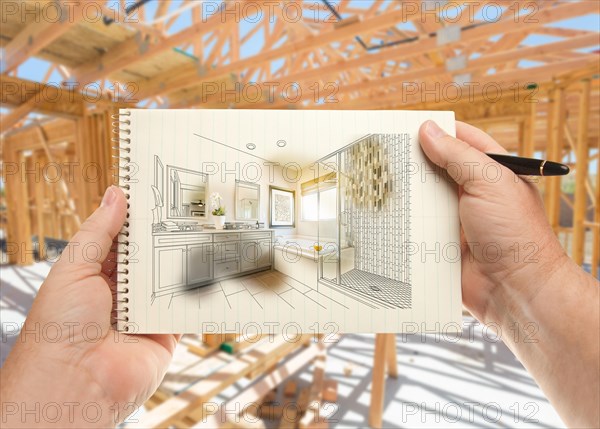 Hands holding pen and pad of paper with bathroom design inside house construction framing