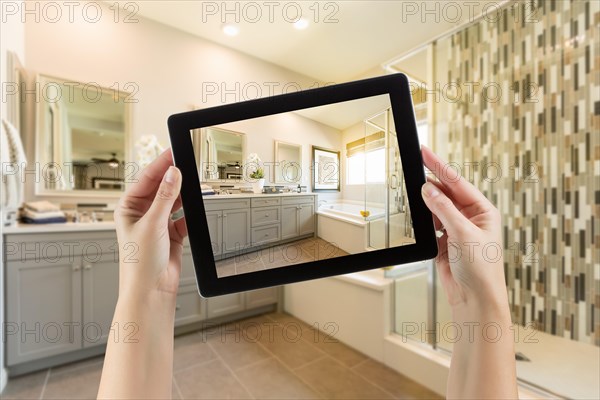 Master bathroom interior and hands holding computer tablet with photo on screen