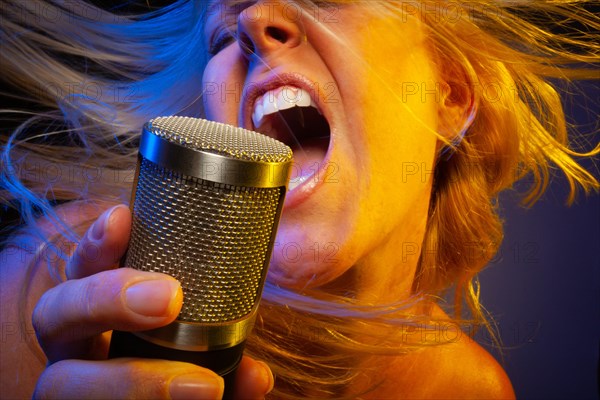 Female vocalist under gelled lighting sings with passion into condenser microphone