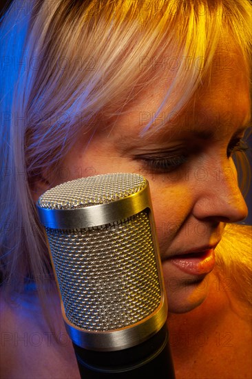 Female vocalist under gelled lighting sings with passion into condenser microphone