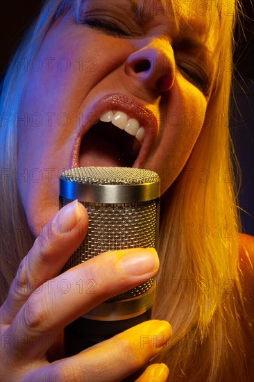 Female vocalist under gelled lighting sings with passion into condenser microphone