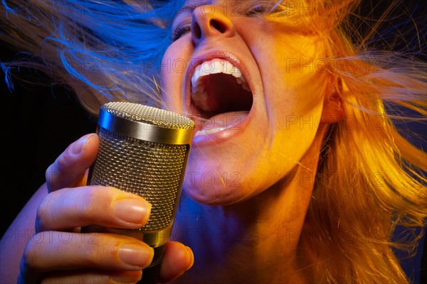 Female vocalist under gelled lighting sings with passion into condenser microphone