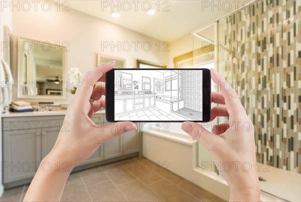 Hands holding smart phone with master bathroom drawing on screen and photo behind