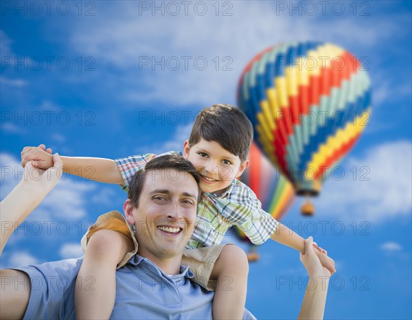Father and son playing piggyback with hot air balloons floating behind them