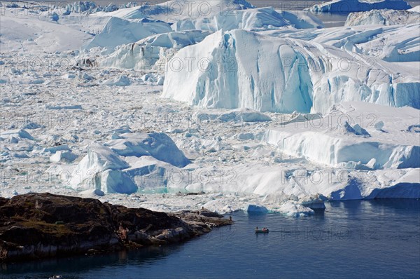 Small fishing boat in front of huge icebergs