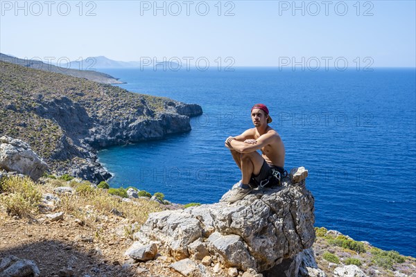 Young man sitting on a rock on the coast