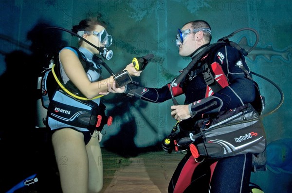 Young woman dives in indoor diving centre Monte Mare and does diving exercises with diving instructor during diving course
