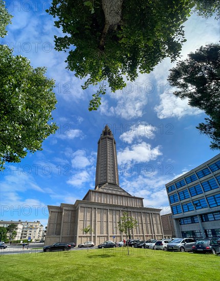 Wide-angle shot of St Joseph's Church with blue sky and framed by trees in Le Havre