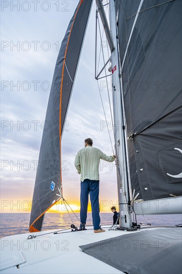 Young man standing leaning against the mast on a catamaran