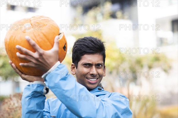 Young man with blue jacket and big pumpkin outside