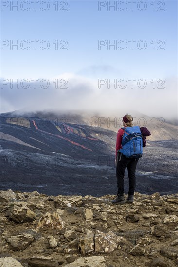 Tourist looking at erupting volcano with lava fountains and lava field